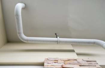A white pipe runs along a ceiling near a stone wall.