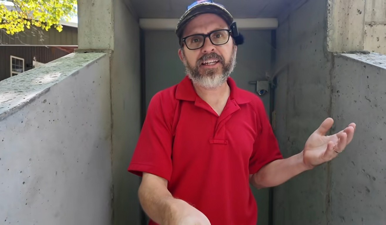 A homesteader standing in front of a storm shelter.