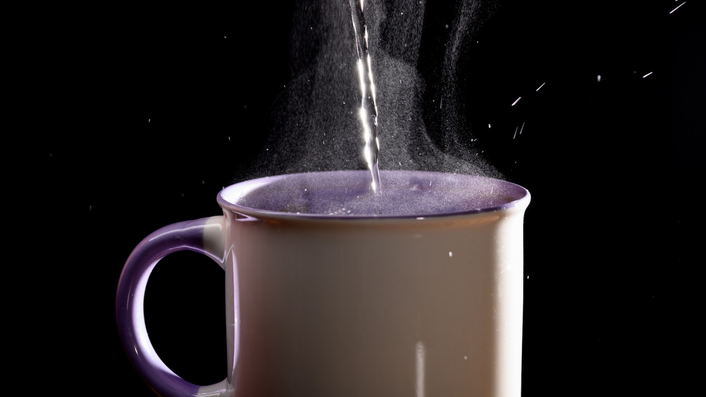 Water is being poured into a cup, creating steam and droplets against a dark background.