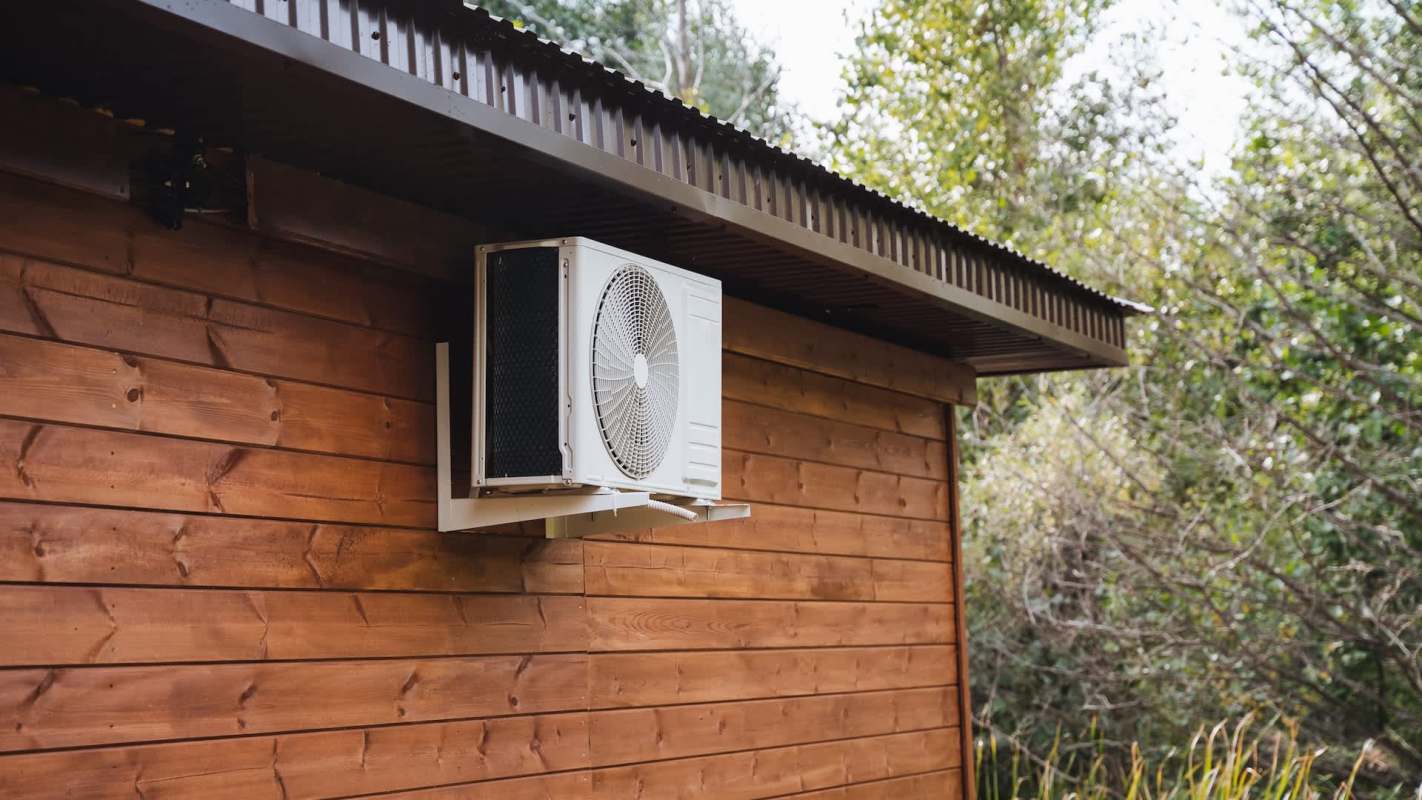 An air conditioning unit mounted on a wooden wall with greenery in the background.