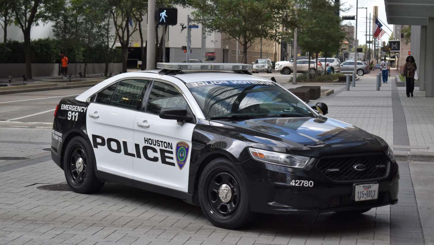 A Houston Police Department patrol car parked on a city street with pedestrians nearby.