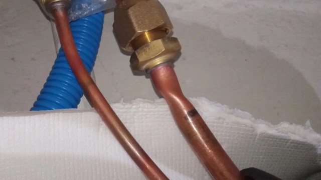 Copper and blue plastic pipes connected with a brass fitting on a white surface.