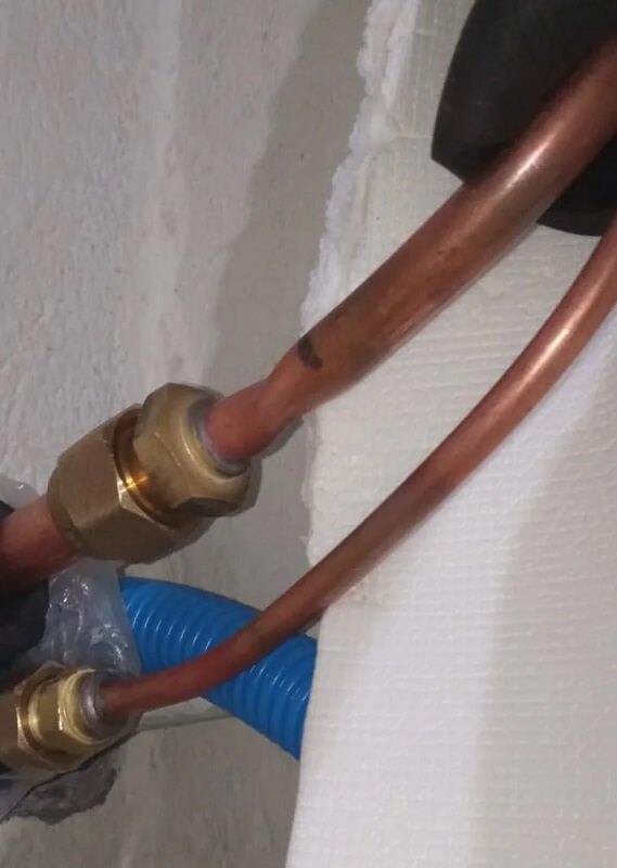 Copper and blue plastic pipes connected with a brass fitting on a white surface.