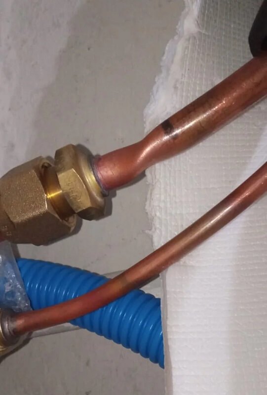 Copper and blue plastic pipes connected with a brass fitting on a white surface.