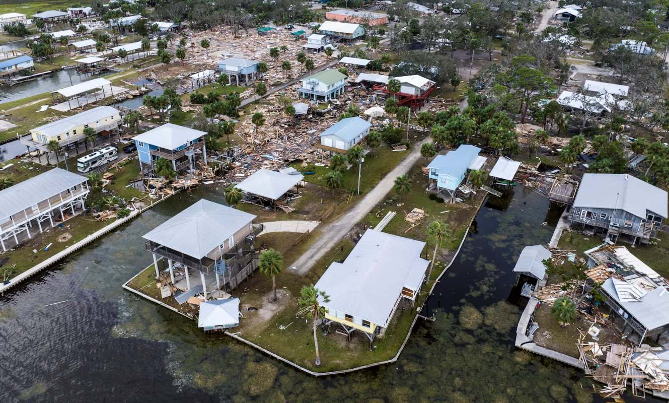 An aerial view of a coastal community showing damaged homes and debris scattered along waterways.