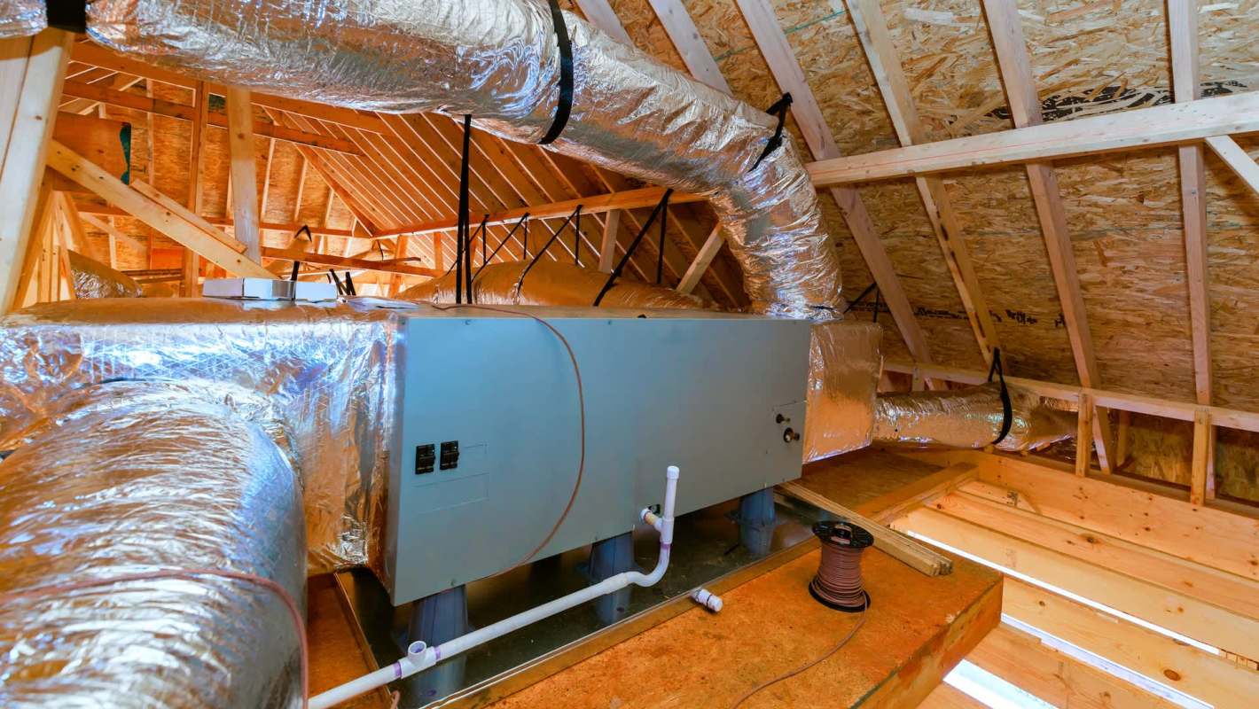 An attic space featuring ductwork and an HVAC unit installed on a wooden floor.