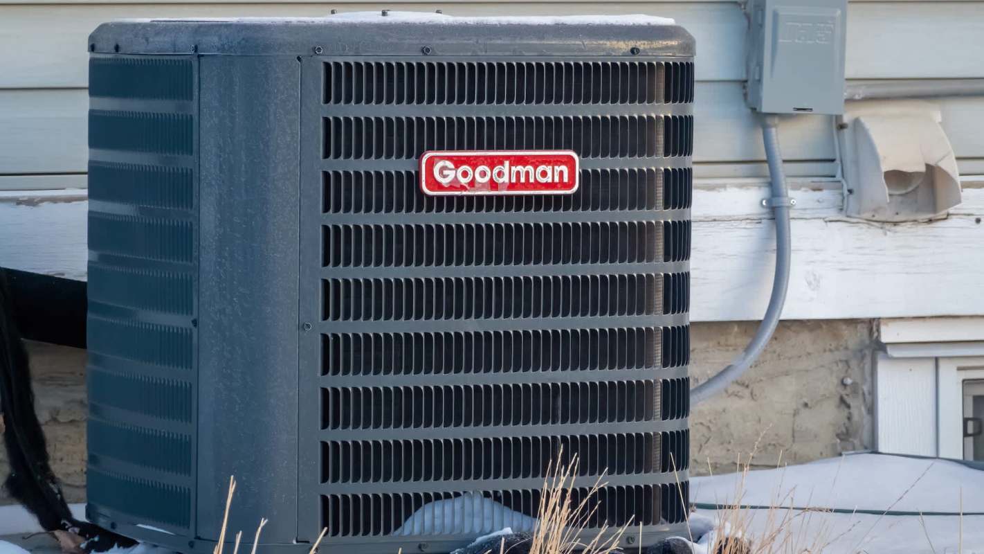 A Goodman air conditioning unit beside a building, with electrical components visible on the wall.