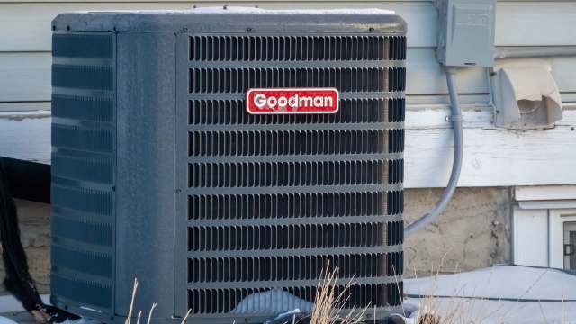 A Goodman air conditioning unit beside a building, with electrical components visible on the wall.