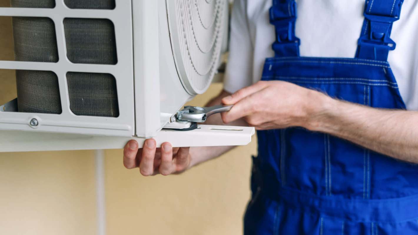 A technician repairs an outdoor air conditioning unit using a wrench.