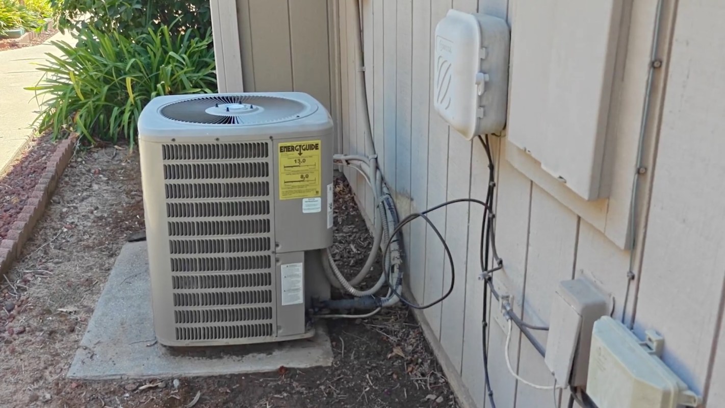 An outdoor air conditioning unit next to a house's exterior wall with electrical and coolant lines connected.