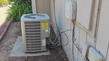 An outdoor air conditioning unit next to a house's exterior wall with electrical and coolant lines connected.
