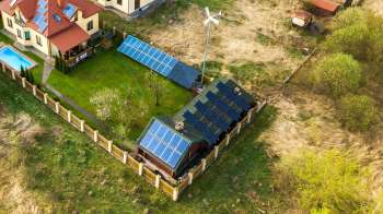 A house and garden featuring solar panels, a wind turbine, and a swimming pool, surrounded by a fence.