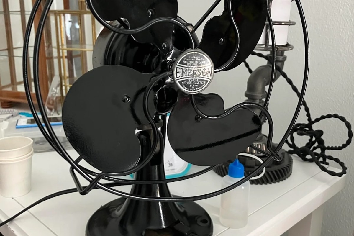 A vintage black Emerson table fan with a circular base and metal blades, displayed on a table with other objects.