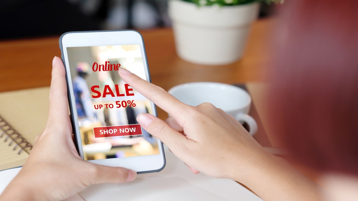 A hand is touching a smartphone screen displaying an online sale advertisement.