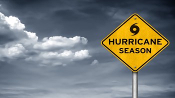 A warning sign for hurricane season against a backdrop of cloudy skies.