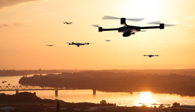 Drones in an orange sky over a city.