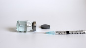 A glass vial with a metal cap beside a syringe on a white surface.