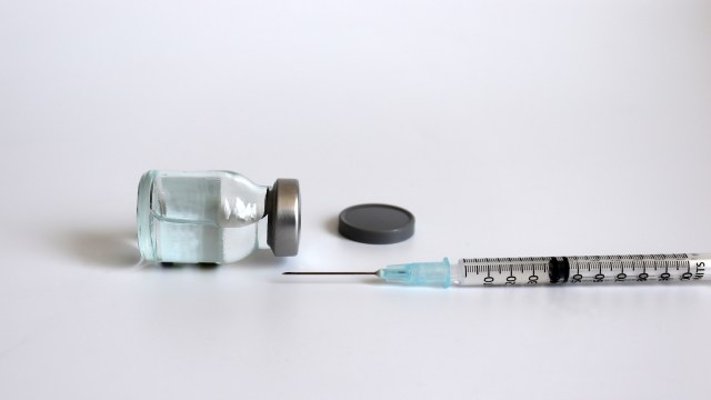 A glass vial with a metal cap beside a syringe on a white surface.