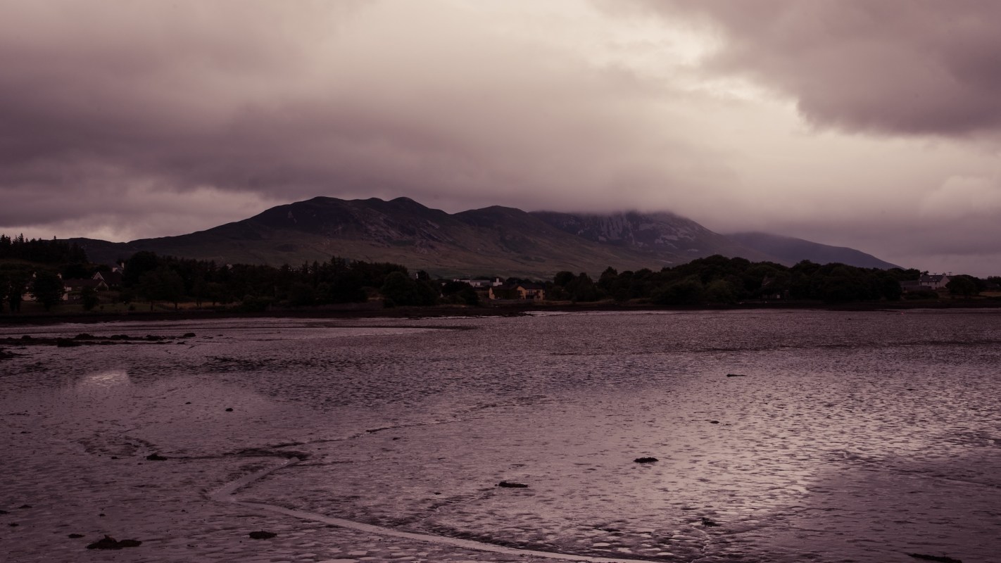 A view of a dry river bed featuring mountains and cloudy skies.