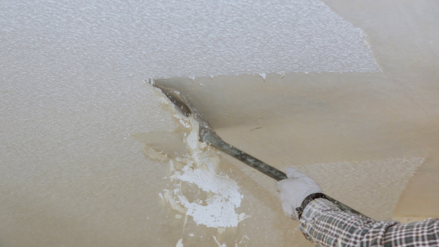 A person removes a popcorn ceiling using a spatula.