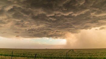 Dark storm clouds over a grassy field with a faint view of a distant storm.