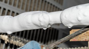 Foam accumulates on a metal pipe, with dripping water and corroded surfaces in the background.