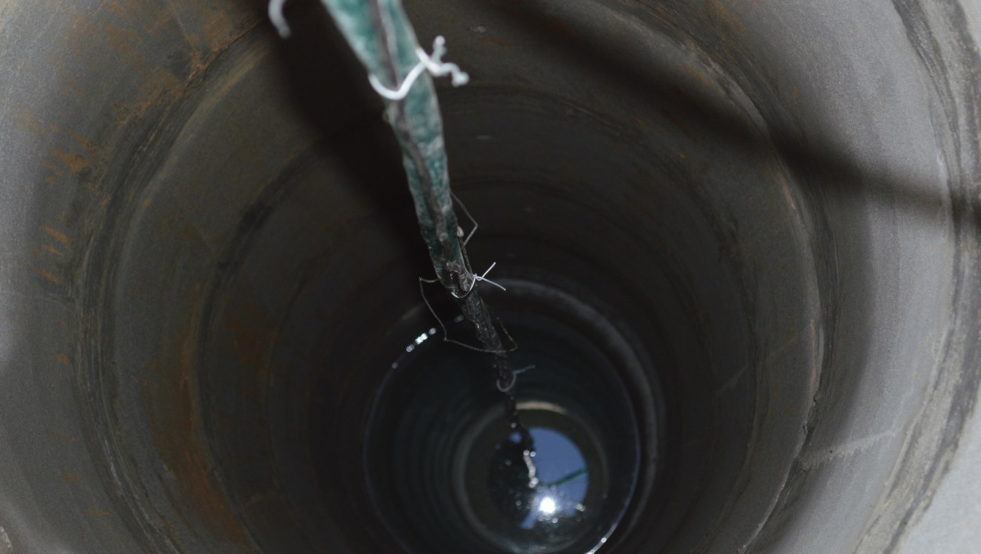 A view inside a deep well with a rope hanging down into the water.