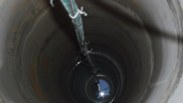 A view inside a deep well with a rope hanging down into the water.
