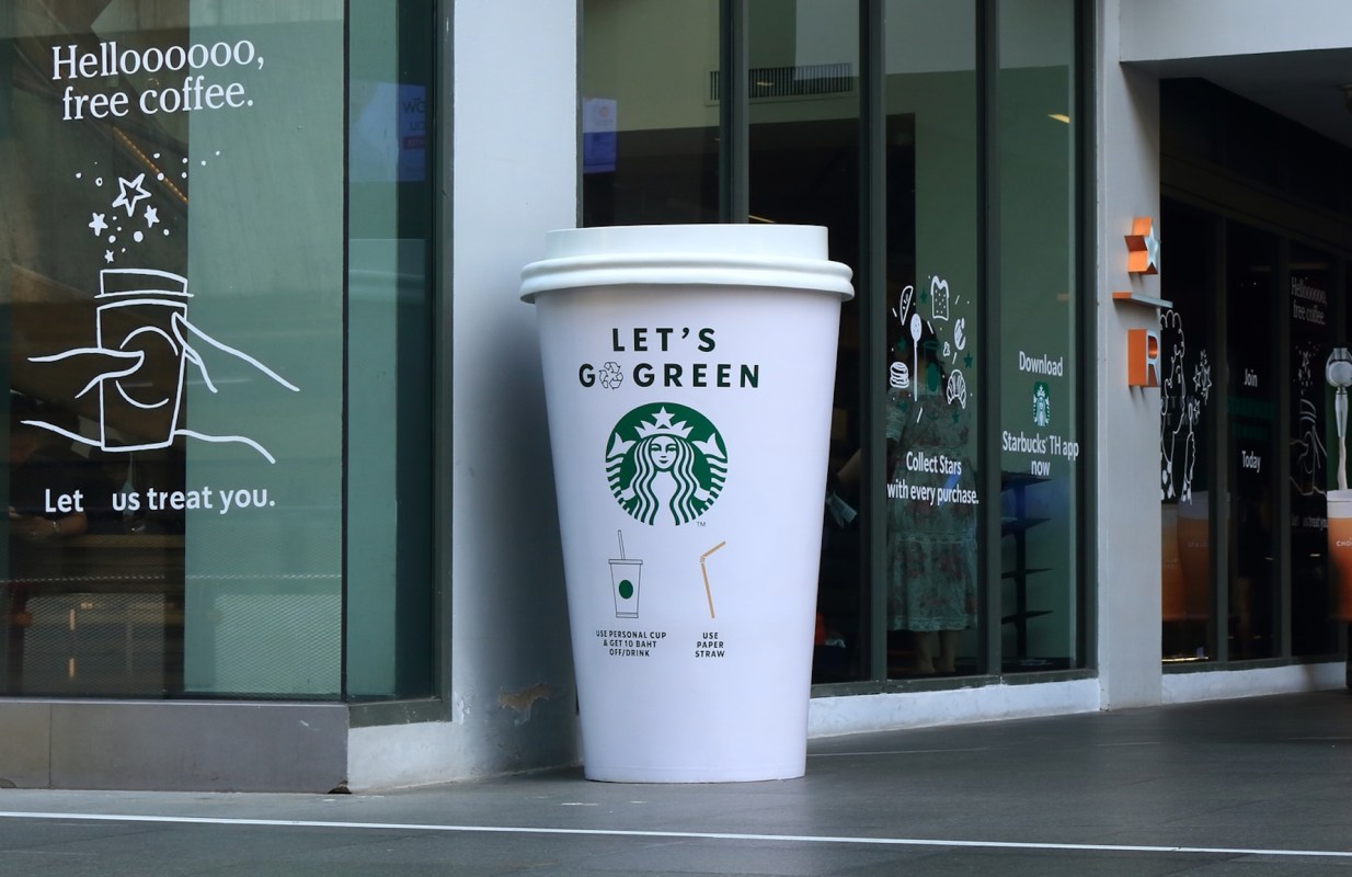 A large promotional Starbucks cup outside a café with green eco-friendly messaging.