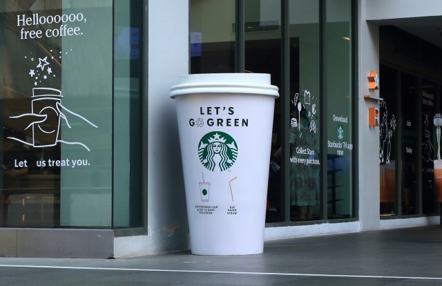 A large promotional Starbucks cup outside a café with green eco-friendly messaging.