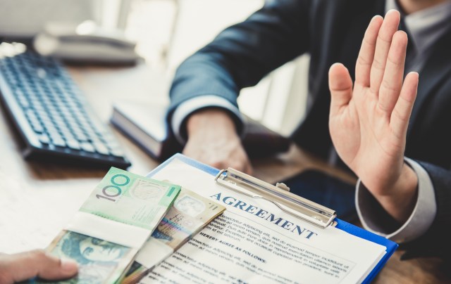 A person gestures with a raised hand while another offers cash and a clipboard with an agreement.