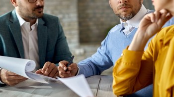 Three people engaged in a meeting, reviewing documents at a table.