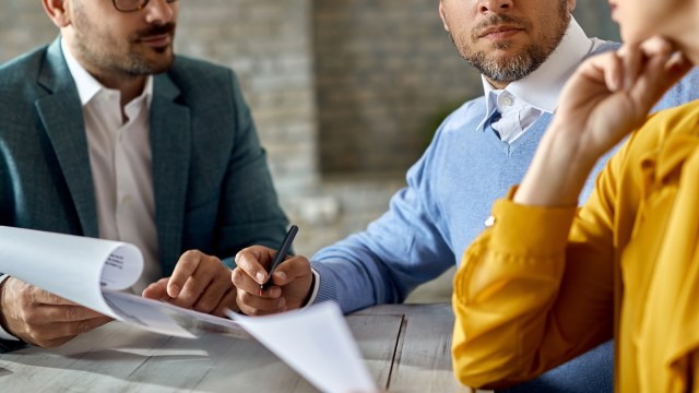 Three people engaged in a meeting, reviewing documents at a table.