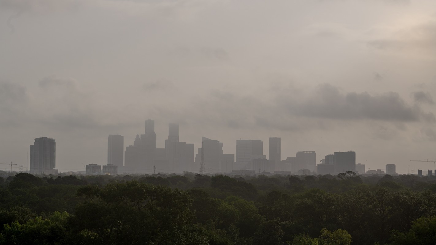 A city skyline obscured by Saharan dust clouds, with trees in the foreground.