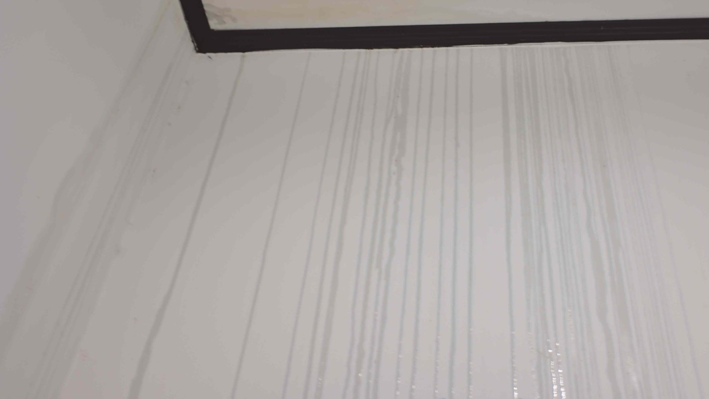 Water stains run down a white wall, with visible vertical lines and a black frame at the top.