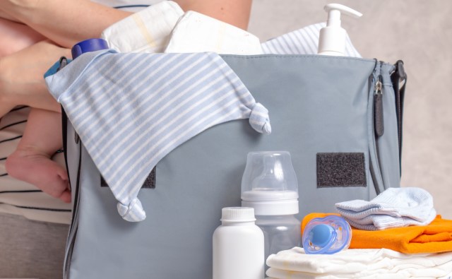 A diaper bag filled with baby supplies including bottles, pacifiers, and clothing.