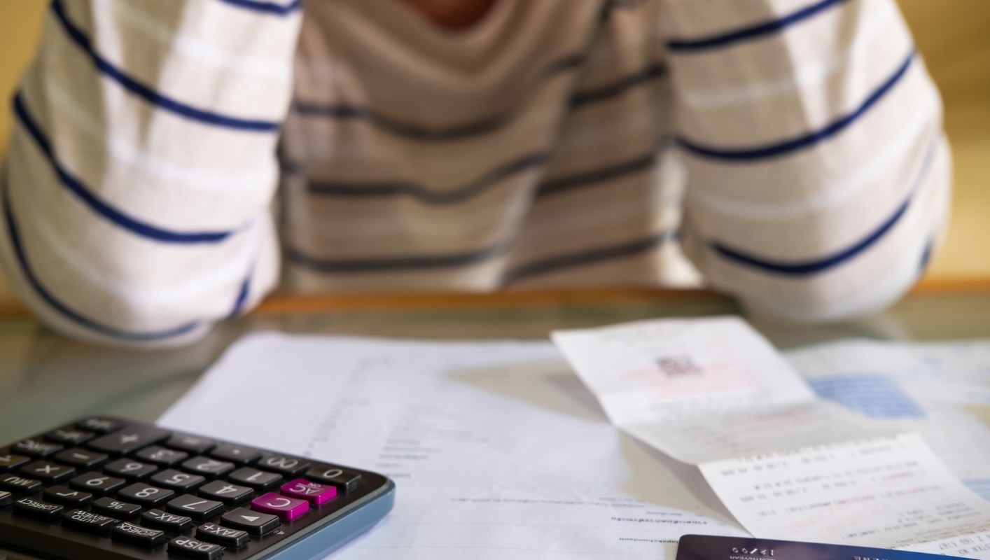 A person with their hands on their head, surrounded by papers, a calculator, and a credit card.