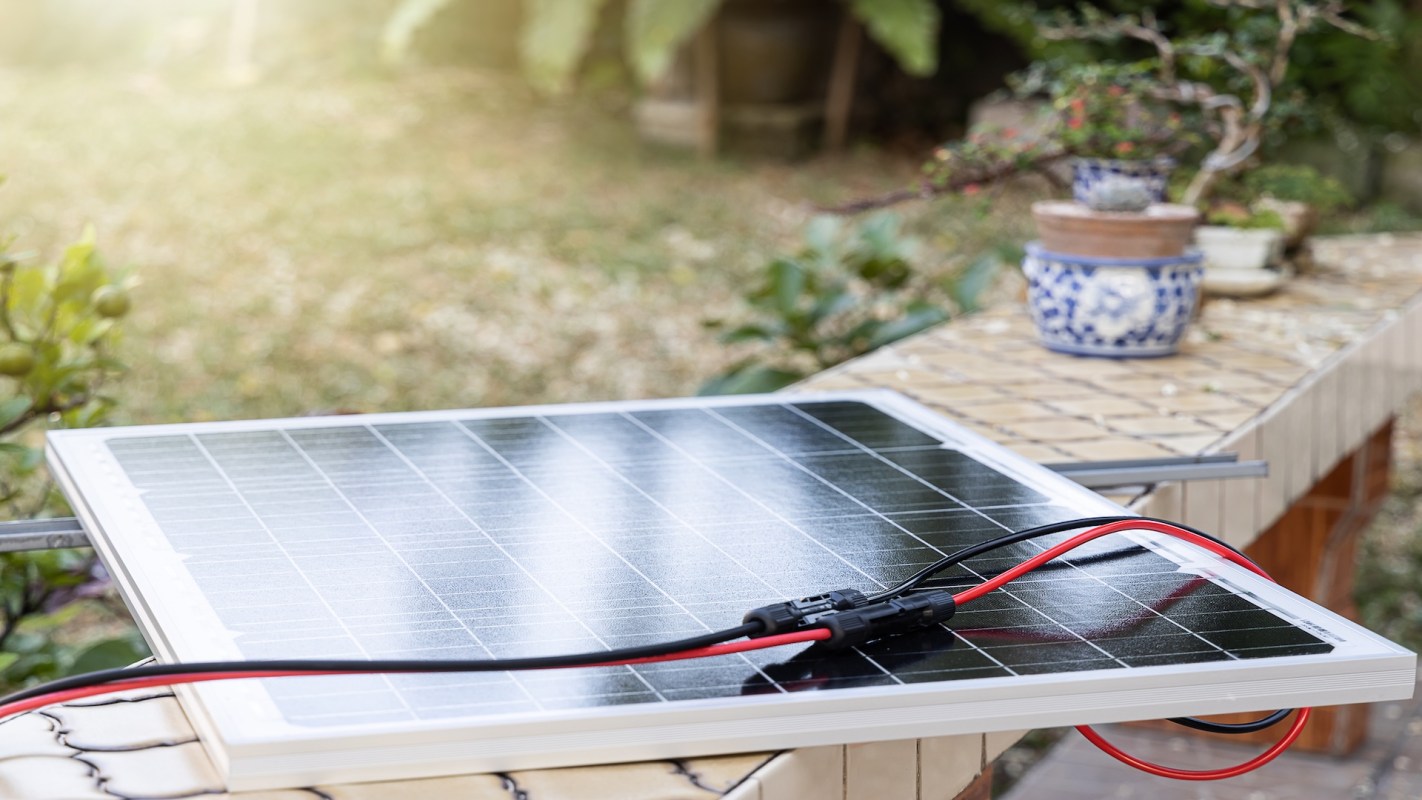 A solar panel with red and black wires on a table in a garden setting.