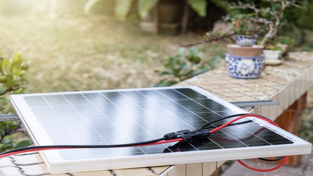 A solar panel with red and black wires on a table in a garden setting.