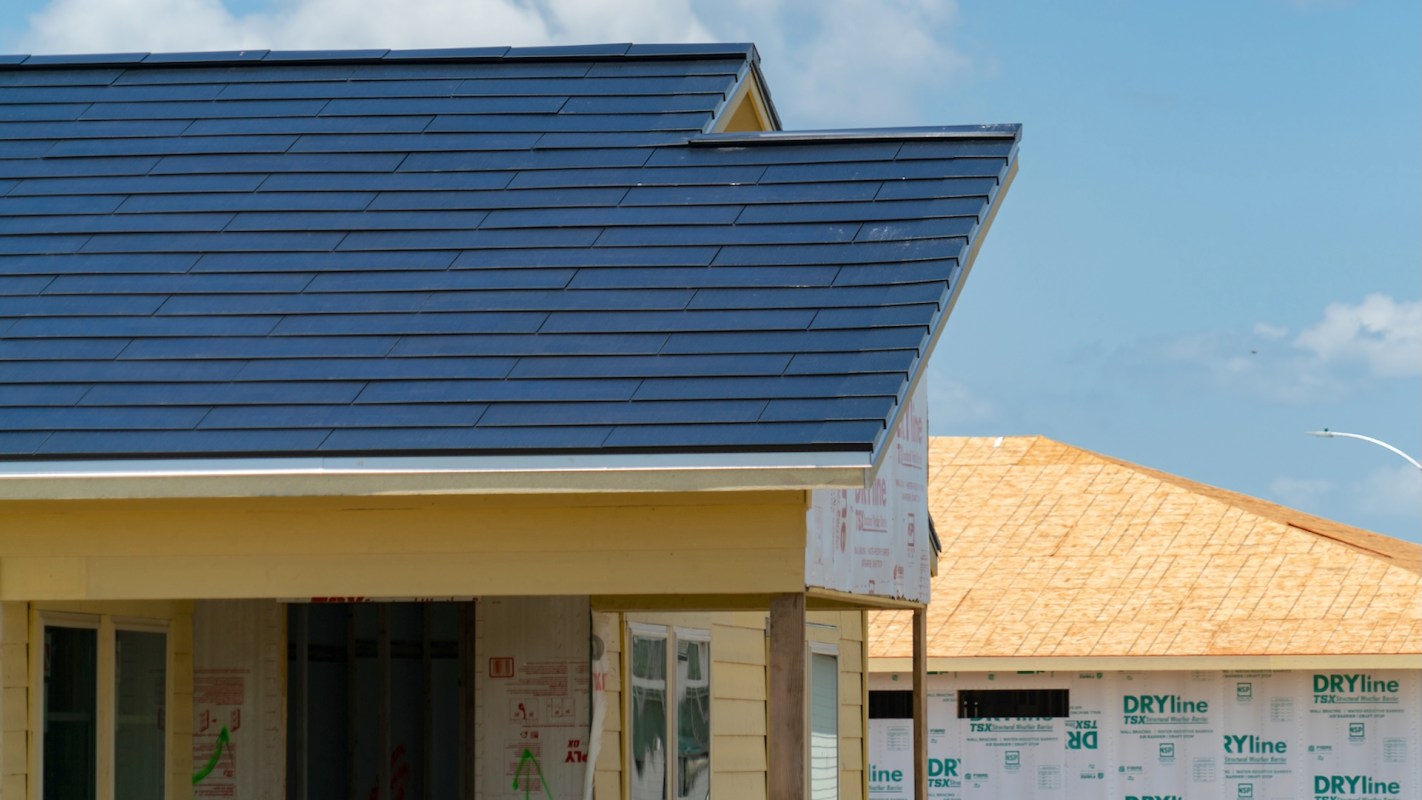 A house under construction with Tesla Solar Roof panels and an adjacent unfinished structure.