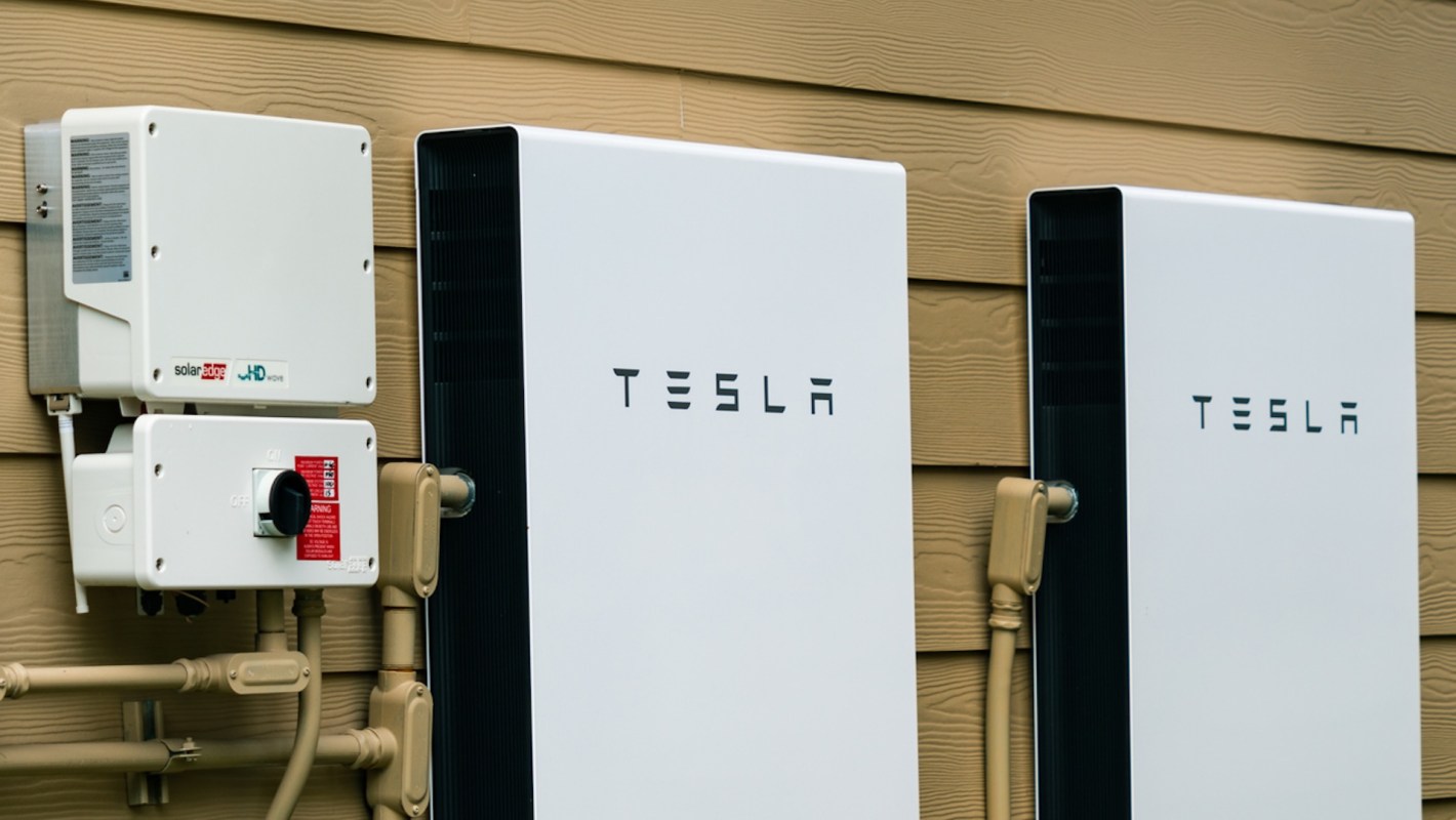 Two Tesla wall-mounted battery units are installed on a wall next to a solar inverter.
