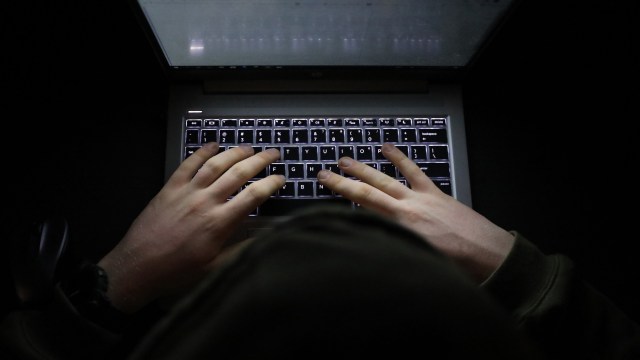 A person types on a laptop keyboard in a dark environment.