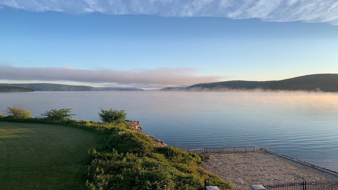 A calm lake surrounded by hills, with morning fog drifting over the water.