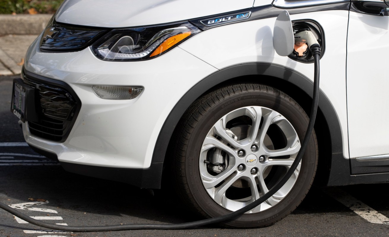 A white Chevrolet Bolt electric vehicle is plugged into a charging station.