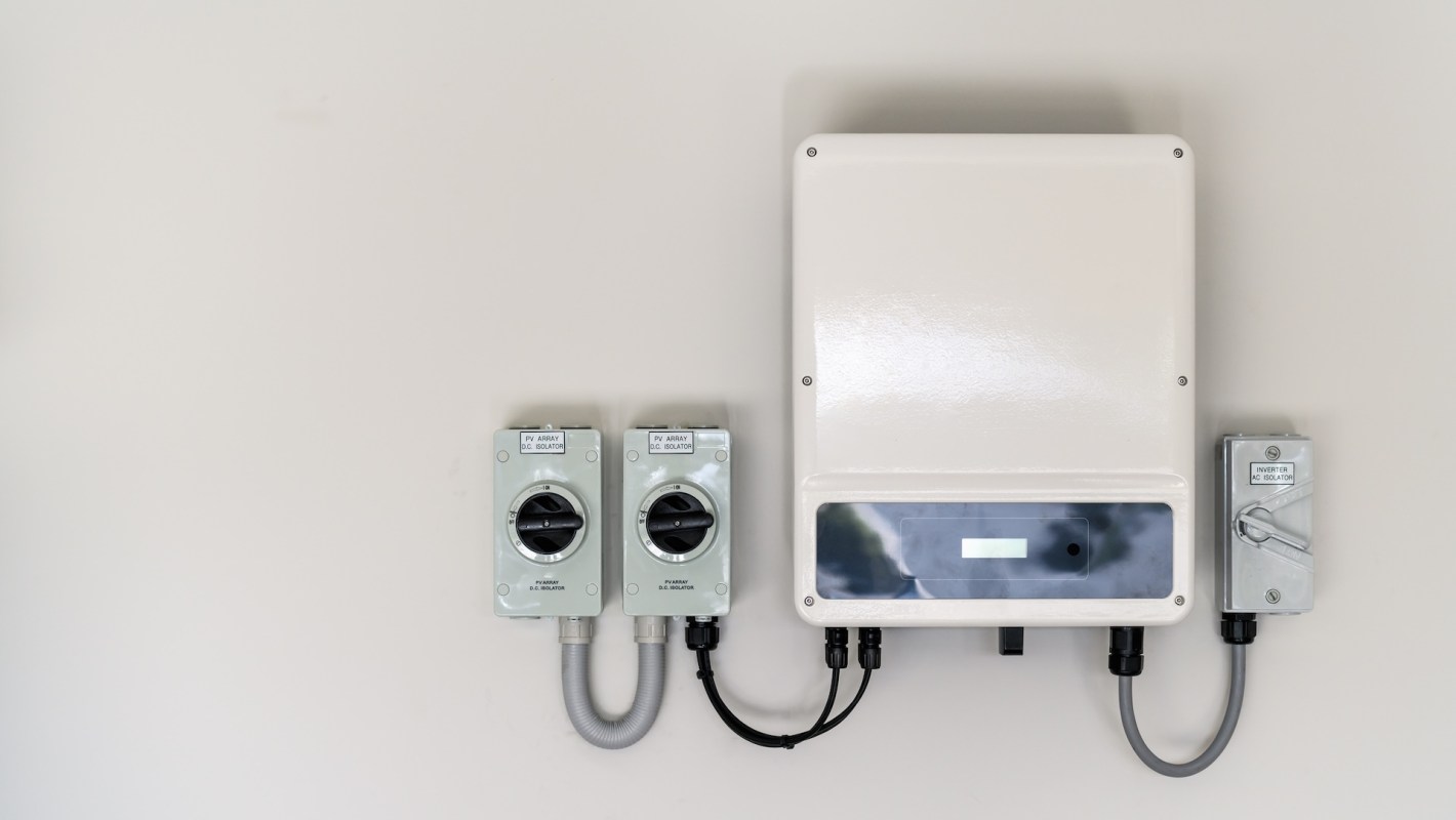 A solar inverter and two DC isolation switches mounted on a wall.