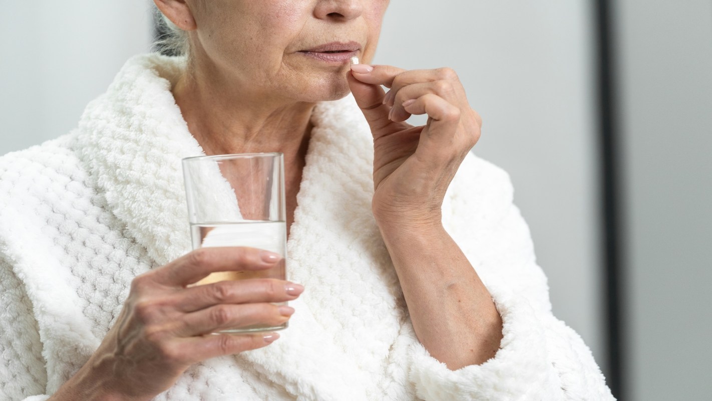 A woman holds a glass of water and a pill while wearing a bathrobe.