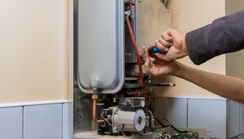 A person uses a tool to work on a mechanical unit mounted on a wall.