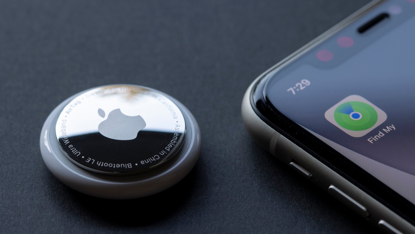 An Apple AirTag next to a smartphone displaying the 'Find My' app.