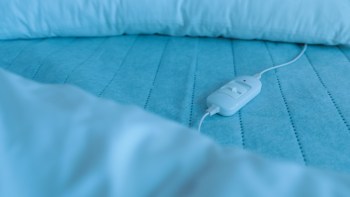 A white control unit for a heating pad on a light blue blanket with a pillow in the background.