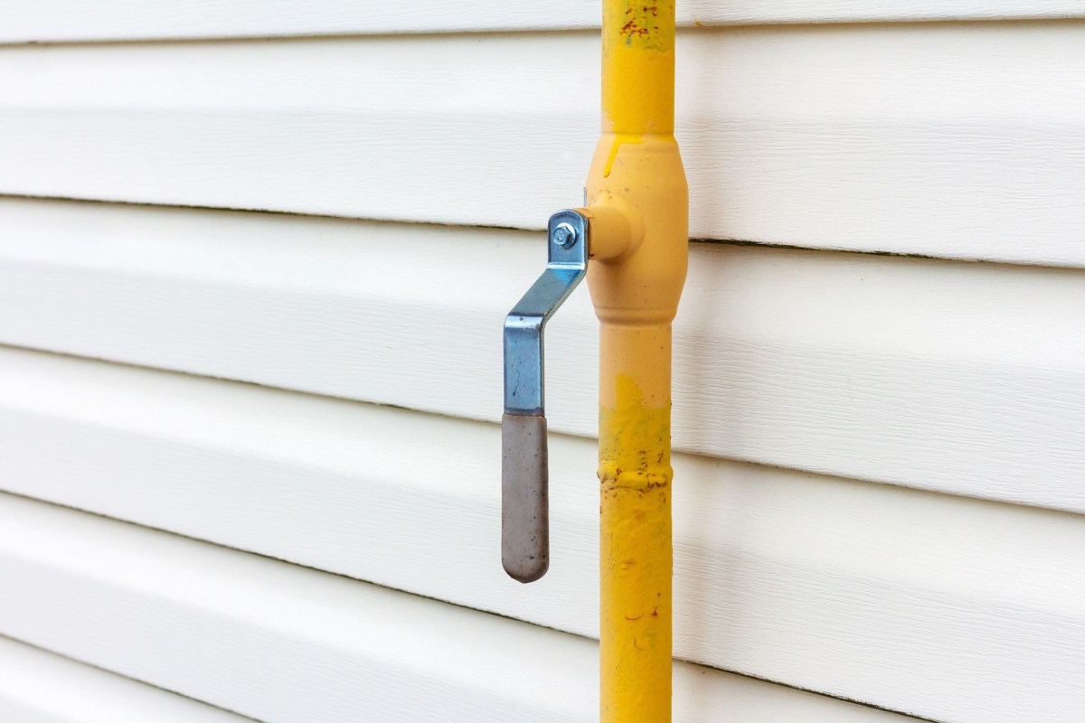 A yellow gas pipe line with a metal handle mounted against white siding.
